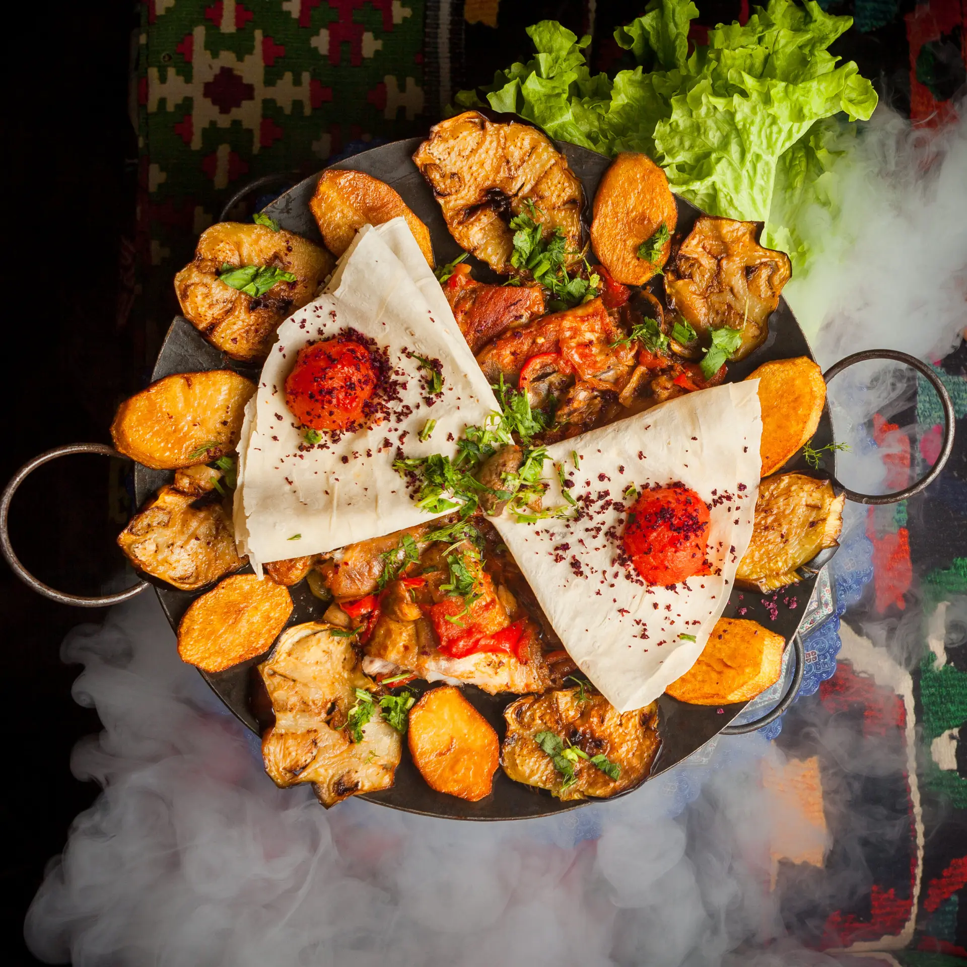 top view chicken sac with fried potatoes and tomato and lavash in smoke on carpet background
