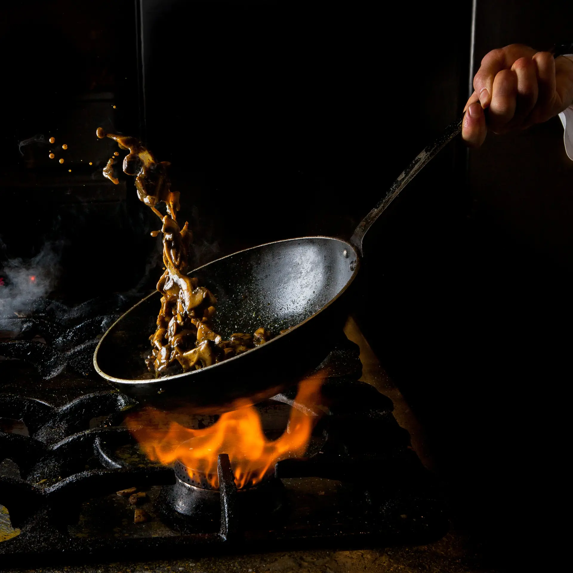 side view mushroom frying with gas stove and fire and human hand in pan on black background
